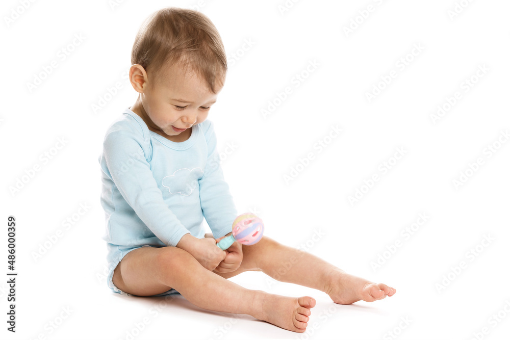 Little boy in romper sitting and playing with plastic rattle.