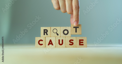 Root cause analysis concept. Define problems to find solution. Business problem solving. Hand holds the wooden cubes with text ROOT CAUSE and magnifying glass icon on grey background,copy space.