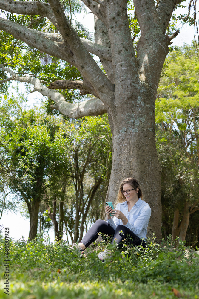 Young woman using a smartphone at day time with a green park in the background. High quality photo Young woman using a smartphone at day time with a green park in the background. High quality photo