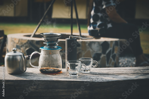 Coffee maker is placed on top of wooden chair in camping area.