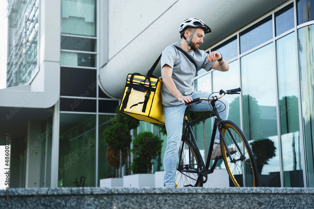 Express delivery courier with insulated bag looking at watch on bicycle.