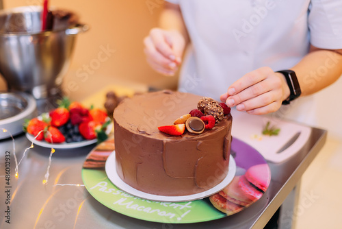 a girl cooks cakes in the kitchen. a pastry chef decorates a chocolate cake with berries  strawberries  blueberries  and sweets