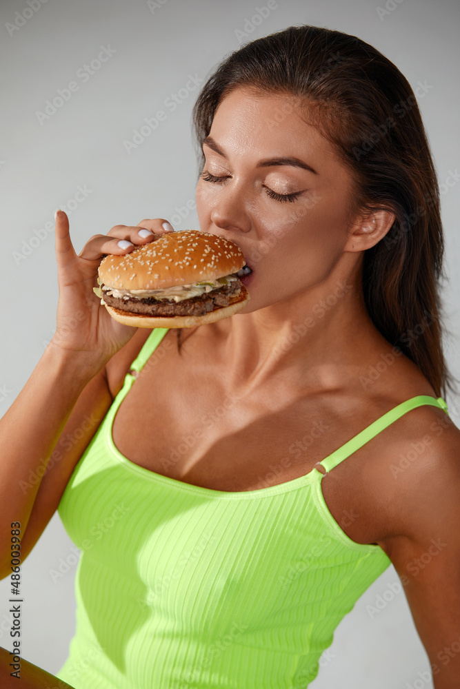 Sporty woman eating unhealthy food on light background. Diet concept Sporty woman eating unhealthy food on light background. Diet concept