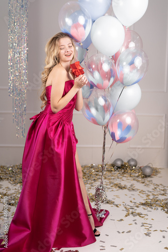 smiling woman in a birthday dress holding a gift box and balloons. cute happy young girl celebrating a birthday.