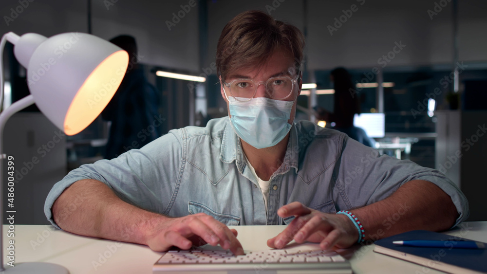 Male executive in safety mask work on computer in modern office