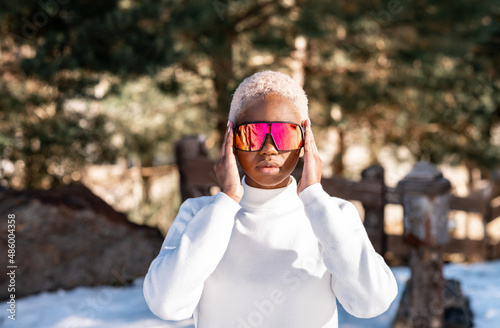 African American woman standing with sunglasses in a snowy park during winter