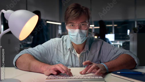 Male executive in safety mask work on computer in modern office