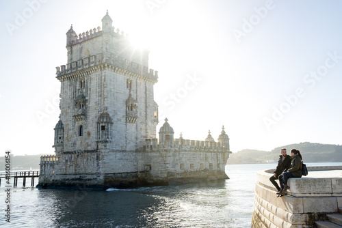 Young woman and man sitting next to the Belem Tower in Lisbon.