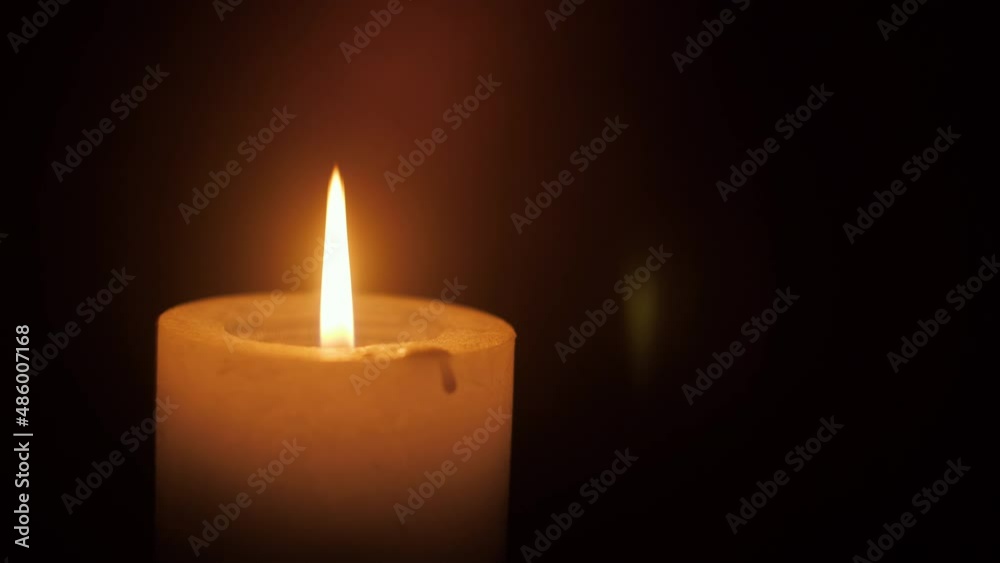 A close-up of a single lit candle with a flickering flame isolated on black background as it spins. A close-up of a single lit candle with a flickering flame isolated on black background as it spins.