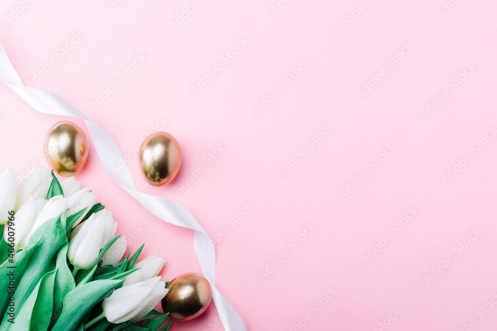 Golden eggs with spring white tulips on pastel pink background in Happy Easter decoration. Foil minimalist egg design, modern top view banner design.