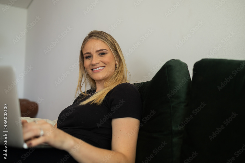 Young woman working at home from her living room couch with laptop on her lap. Home office concept. Young woman working at home from her living room couch with laptop on her lap. Home office concept.