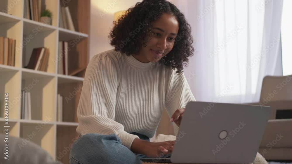 Internet fun. Remote work. Online communication. Joyful typing woman chatting with friend at laptop enjoying weekend indoors at home living room.