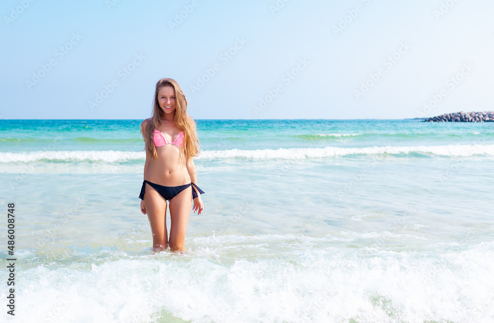 Young attractive blonde girl with perfect sport body in bikini on the tropical summer beach