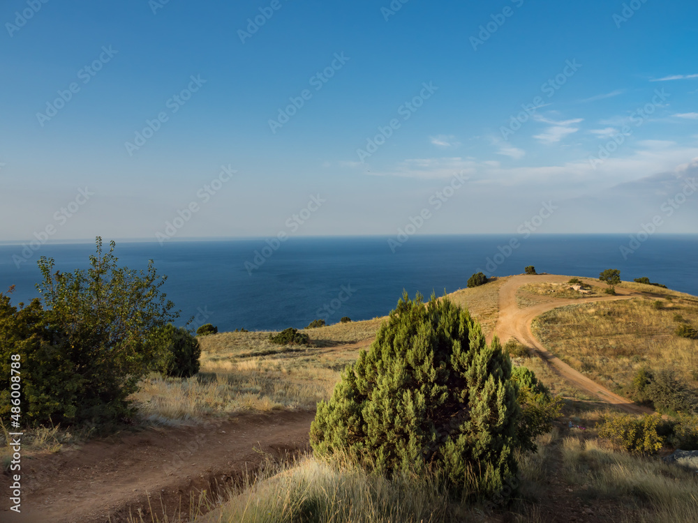 View from the top of the mountain to the meadow with dry grass and the blue sea. Dawn on the mountain. Mountain sandy trails. Wallpaper