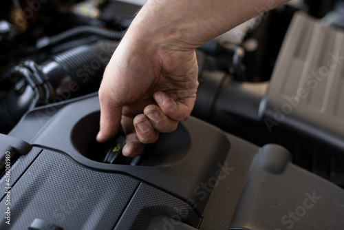 A close up of the man's hand checking the oil in the car engine