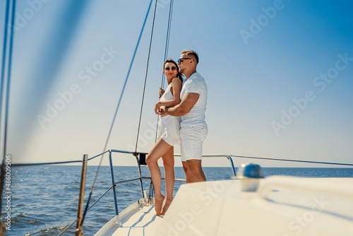 happy young couple in white clothing standing together on yacht while looking at the blue sea