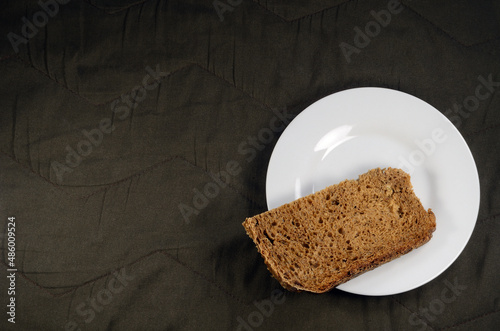 Fresh rye bread on a white saucer, brown fabric background.