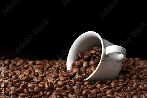 coffee beans spill out of a white ceramic cup, dark background
