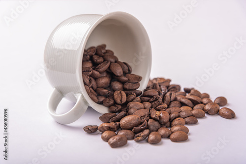 coffee beans spill out of a white ceramic cup
