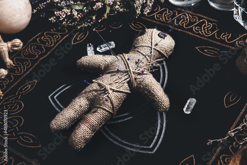 Voodoo doll pierced with pins surrounded by ceremonial items on table. Curse ceremony