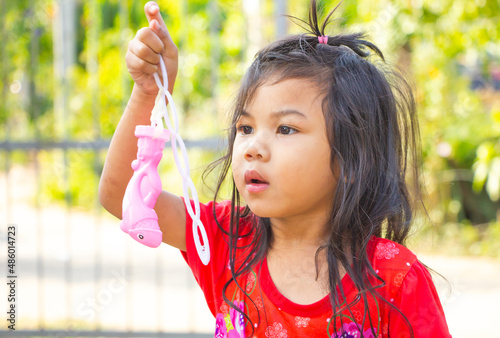 Cute little asia girl hold blowing a soap bubbles toy at outdoor and looking to you. cute messy hair girl