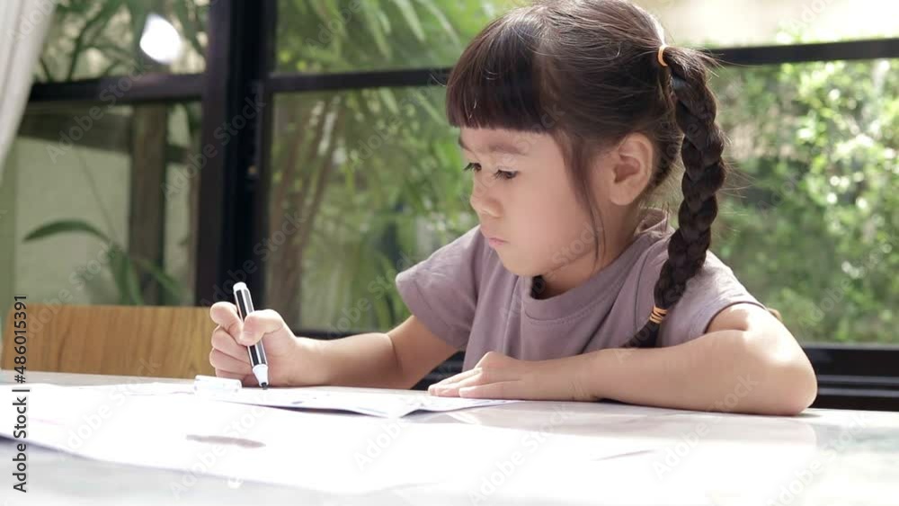cute little asian girl sitting on the table Drawing and coloring on paper at home. Children's education concepts. online learning from home cute little asian girl sitting on the table Drawing and coloring on paper at home. Children's education concepts. online learning from home