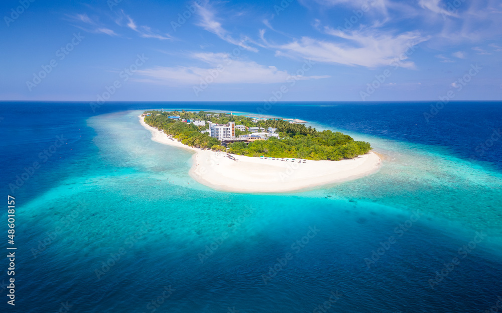Tropical island with white beach and turquoise water in Maldives. Idyllic summer holidays vacation destination. Luxury hotel resort. Warm sunny day with blue sky. Aerial drone panorama.