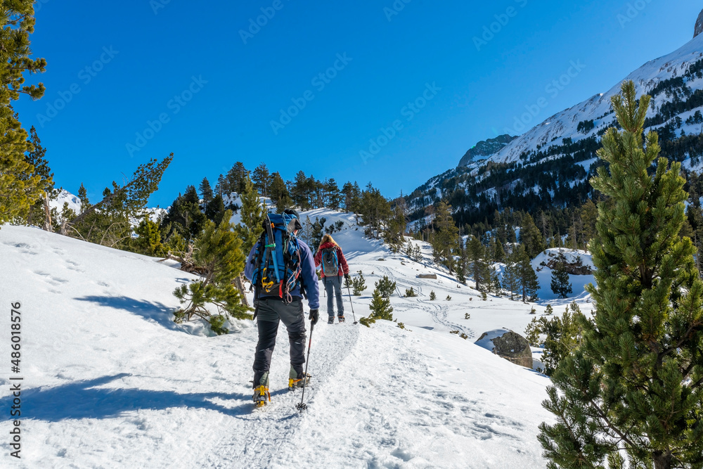 Two people, man and woman, walking with snowshoes and crampons up the mountain. Mountaineering, alpinism. Snowy landscape of the Pyrenees.