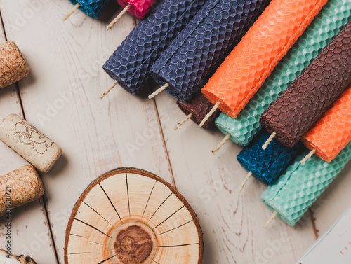 Multicolored beeswax candles with honeycomb texture on a wooden floor. Tree cuts and other accessories.