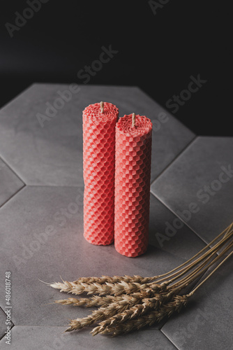 Two pink textured beeswax candles stand on a gray ceramic tile on a black background.