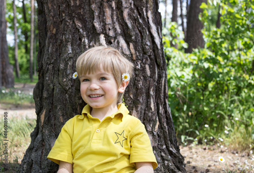 cute smiling boy sitting near a tree. Summer mood, carefree joyful child portrait. happy childhood, walks outdoors