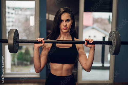 Beautiful athletic woman lifting barbell while training in the gym