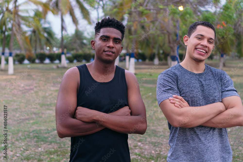 Two friends in sportswear, standing in a park, smiling with their arms crossed. Two friends in sportswear, standing in a park, smiling with their arms crossed.