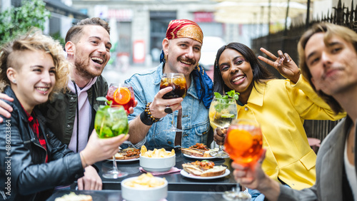 Lgbt group of diverse people sitting at bar, happy friends taking a selfie at the restaurant drinking cocktails, social media and inclusion concept