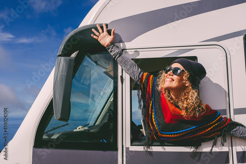 Overjoyed young adult woman oustretching arms outside the windows of a camper van and celebrate freedom and summer holiday travel vacation lifestyle