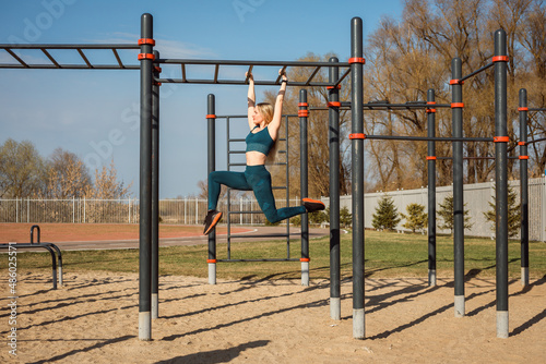 Athletic woman is doing acrobatics elements on the horizontal bar outdoors in spring.