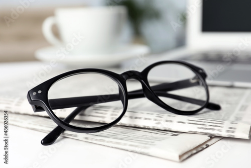 Newspapers and glasses on white table indoors, closeup