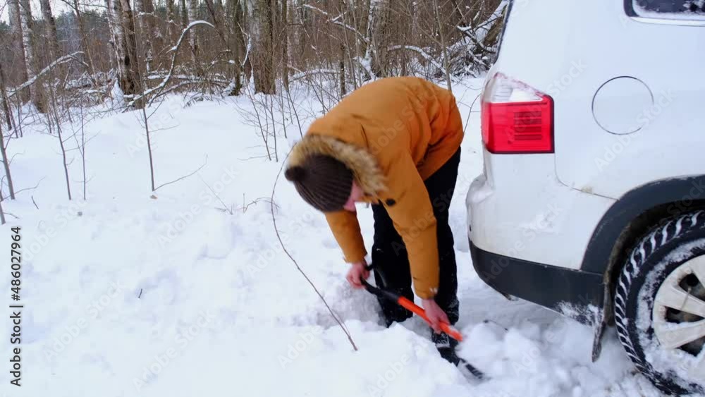 Man digs out stalled car in snow with car shovel. Transport in winter got stuck in a snowdrift after a snowfall, sat on bottom. First aid, tow truck, winter tires spikes and all-season. Slow motion