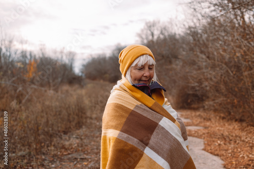 Middle age beautiful female traveler posing with knitted scarf enjoying warm sunny weather in autumn season