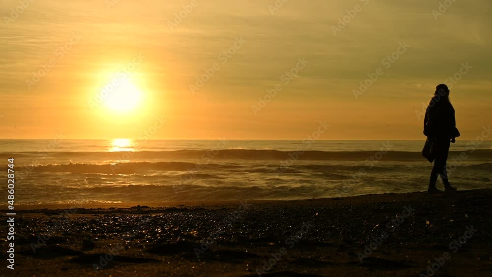 Caucasian Woman Walking Alone Along the Beach During Scenic Sunset Caucasian Woman Walking Alone Along the Beach During Scenic Sunset