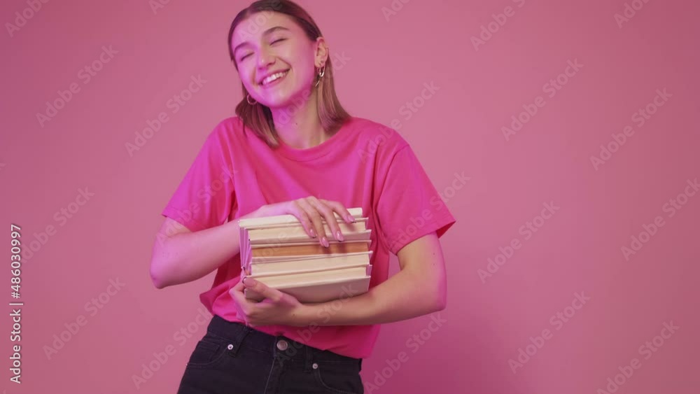 Funky student. Book fair. I love reading. Excited happy woman funny dancing with pile of bestseller textbooks isolated on pink studio background. Funky student. Book fair. I love reading. Excited happy woman funny dancing with pile of bestseller textbooks isolated on pink studio background.