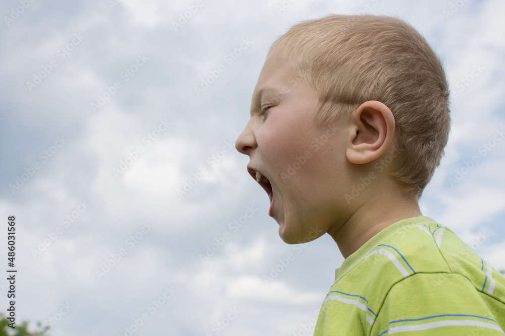 angry boy screaming,little boy with closed eyes screams in nature, boy turned to the side