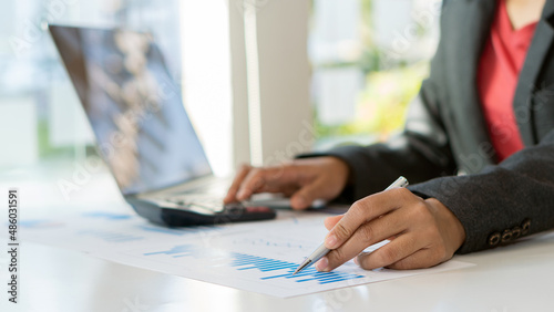 Businessman hand holding pen pointing to marketing graph and working on laptop computer and a calculator to calculate work concepts online