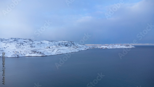 Winter seascape. A snow-covered fishing village in the far north. Sea and blue sky. Russia  Teriberka  Kola Peninsula. Top view.