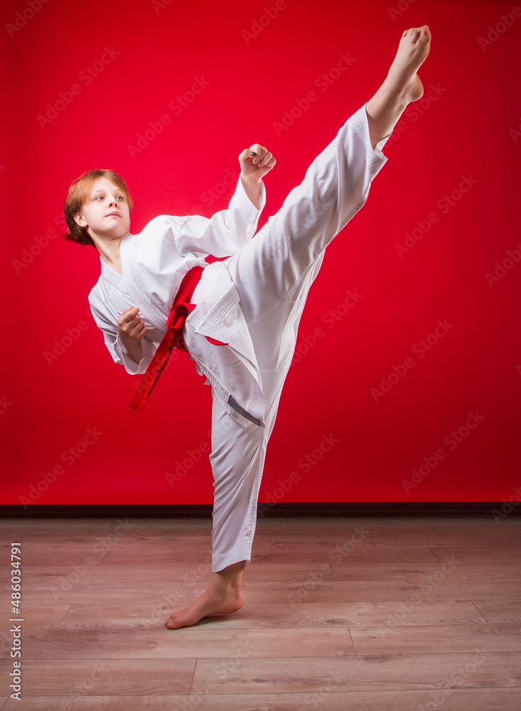 young girl karateka in a white kimono and a red belt trains and performs a set of exercises on a bright red background