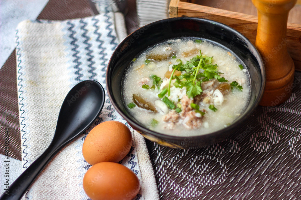 Pork boiled rice with shiitake mushrooms on a black bowl with a spoon on the table.