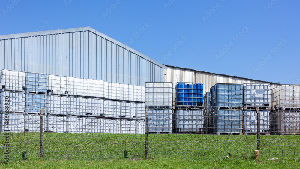 Industrial Chemical Holding Tanks With Metal Cage for safe transportation of liquids stacked outdoors in blue sky Industrial Chemical Holding Tanks With Metal Cage for safe transportation of liquids stacked outdoors in blue sky
