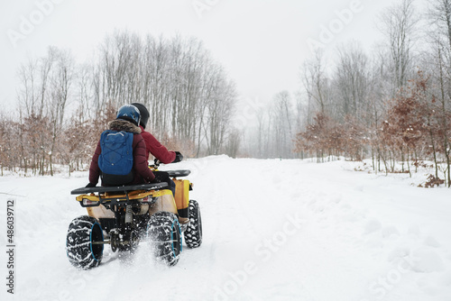 Man on a quad bike next to a woman. Young couple doing outdoor winter activities, riding an ATV in snowy forest