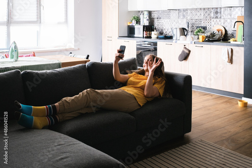 Young woman lying on the couch and using smartphone for speak with friends and relatives.