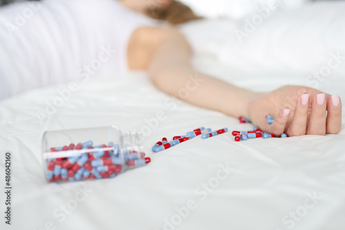 Dead woman lying on bed with scattered medical capsules closeup